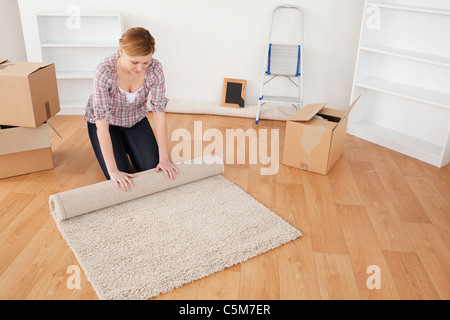 Cute femme rouler un tapis pour se préparer à un déménagement Banque D'Images