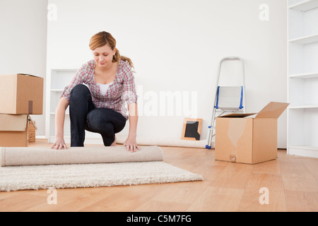 Femme charmante rouler un tapis pour se préparer à un déménagement Banque D'Images