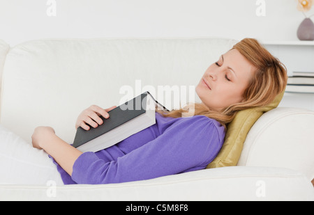 Belle femme allongée sur le canapé qui s'est endormie en lisant un livre Banque D'Images