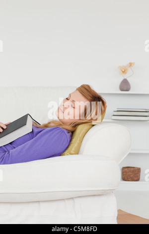 Jolie femme allongée sur le canapé qui s'est endormie en lisant un livre Banque D'Images