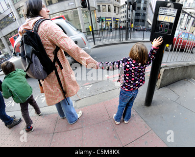 Londres, Angleterre, Royaume-Uni. Jeune fille en appuyant sur le bouton de passage de piétons et holding mother's hand Banque D'Images