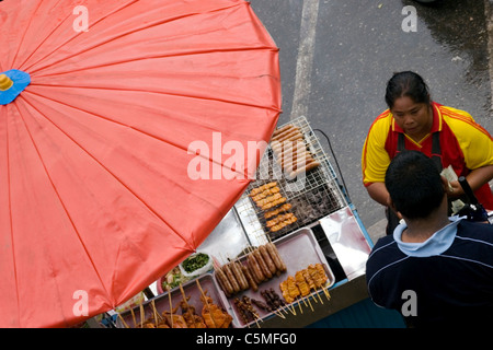 Une femme vend un assortiment de grillades sous un grand parapluie à un marché de l'alimentation de rue dans le Nord de la Thaïlande. Banque D'Images