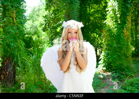 Enfants Angel girl smelling roses fleurs en forêt avec des ailes blanches et couronne Banque D'Images