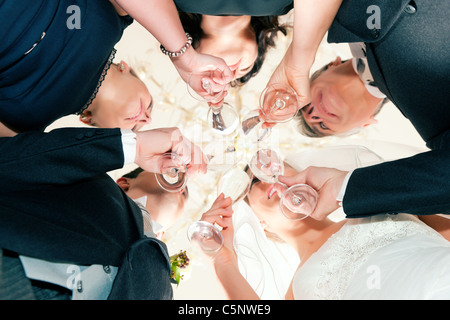 Fête de mariage mariée, marié et père épouse clinking glasses avec vin mousseux debout sous un lustre, close-up Banque D'Images