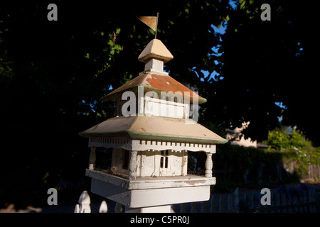 Maison d'oiseau blanc avec toit en métal et d'un drapeau en haut près de trottoir. Banque D'Images