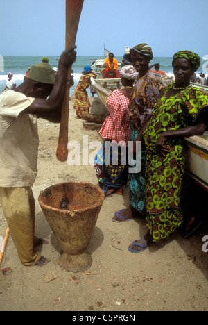 Un homme battre la farine de poisson avec les femmes en robe colorée sur une plage d'Afrique de l'Ouest Banque D'Images