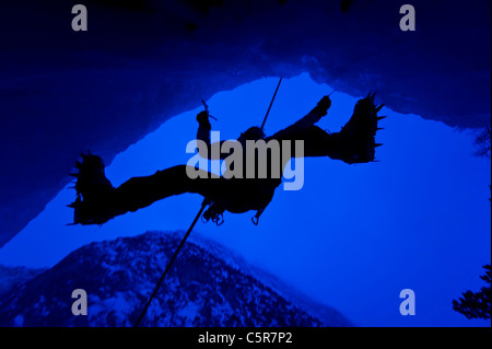 Grimpeur sur glace dans la grotte avec vue sur la montagne derrière. Banque D'Images