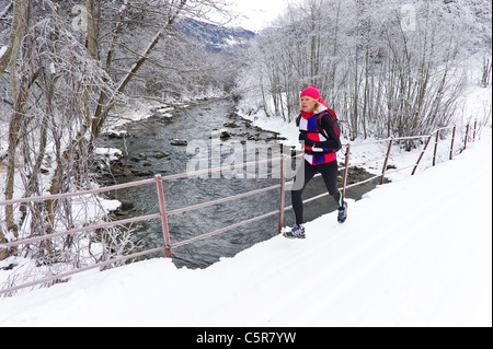 Une femme le jogging sur un pont sur une rivière d'hiver enneigé. Banque D'Images