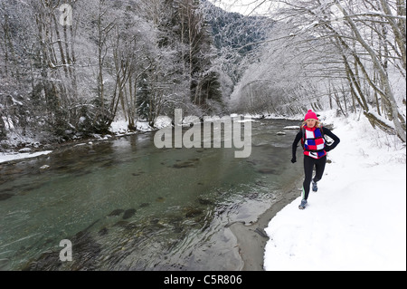 Un jogger qui longe une rivière alpine enneigée. Banque D'Images