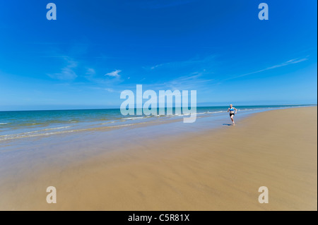 Une femme en marche pieds nus le long d'une vaste plage de sable pieds nus à côté de l'Océan Banque D'Images