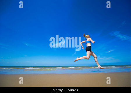 Un athlète barefoot jogging le long d'une plage de l'océan de sable. Banque D'Images