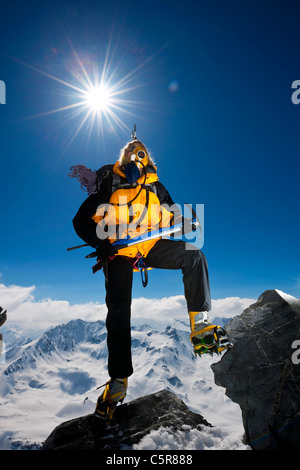 L'alpiniste grimpe sur les rochers, sur la montagne enneigée très élevé au-dessus des nuages. Banque D'Images