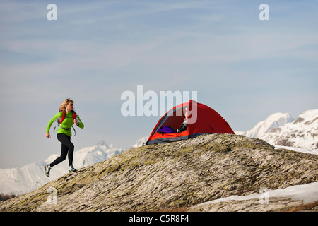 Une femme s'exécute en arrière à sa tente dans les montagnes de haute altitude. Banque D'Images