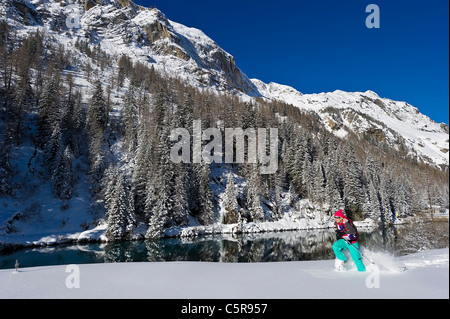 Une femme qui traverse une profonde poudreuse en raquettes passé de superbes montagnes enneigées et le lac. Banque D'Images