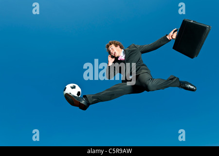 Un homme d'affaires de soccer ball salves tandis que sur téléphone portable. Banque D'Images