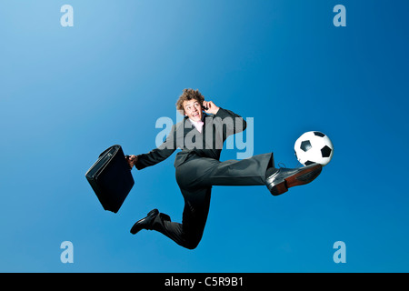 Un homme d'affaires de soccer kicks la balle alors que sur téléphone portable. Banque D'Images