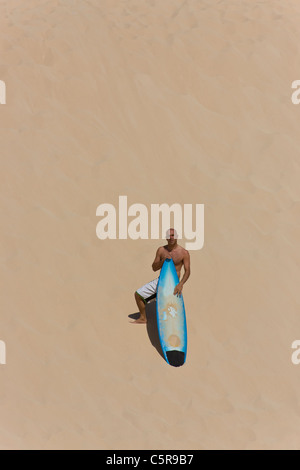 Surfer se dresse sur dune avec planche de surf. Banque D'Images