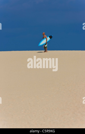 Un surfeur debout sur une dune de sable avec surf. Banque D'Images