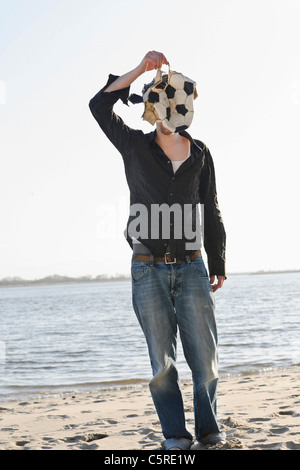 Allemagne, Hambourg, Mid adult man couvrant son visage déchiré avec football près de fleuve d'Elbe Banque D'Images