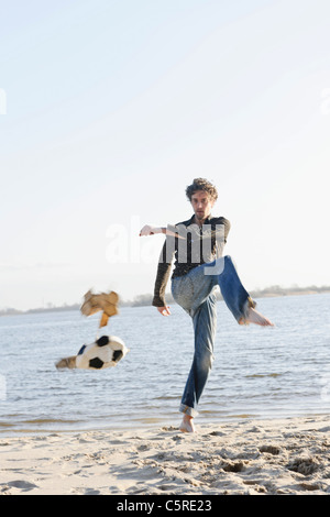 Allemagne, Hambourg, Mid adult man kicking football près de la rivière Elbe déchiré Banque D'Images