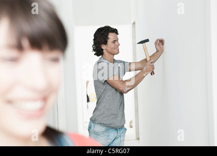 Germany, Cologne, Young man hammering nail dans la rénovation d'appartement avec femme en premier plan Banque D'Images