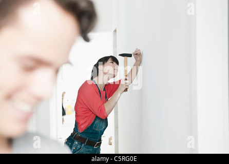 Germany, Cologne, young woman hammering nail dans la rénovation d'appartement avec l'homme en premier plan Banque D'Images