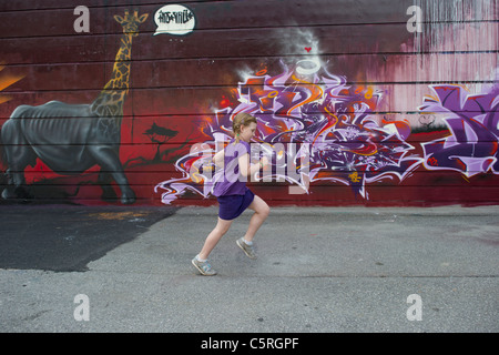 Une jeune fille portant un violet passé en courant du bâtiment mur recouvert de graffitis à Chamonix Mont Blanc, France. Banque D'Images