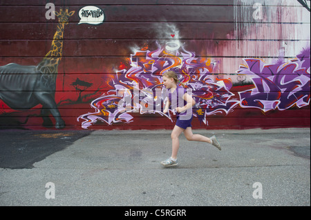 Une jeune fille portant un violet passé en courant du bâtiment mur recouvert de graffitis à Chamonix Mont Blanc, France. Banque D'Images