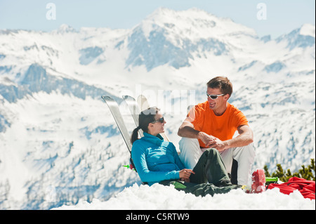 L'Autriche, Pays de Salzbourg, Altenmarkt-Zauchensee, Mid adult couple assis et s'appuyant sur des skis en hiver neige Banque D'Images