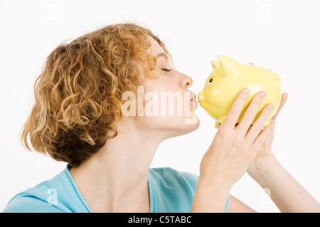 Young woman kissing piggy bank, side view, portrait Banque D'Images