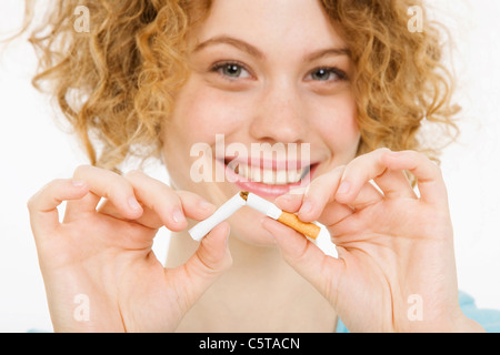 Jeune femme breaking cigarette à moitié, smiling, portrait Banque D'Images