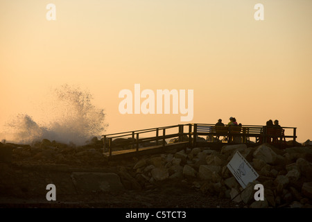 Les touristes regarder le coucher de soleil comme de grandes vagues de l'Atlantique Sud s'écraser sur les brise-lames à côté de la plage. Swakopmund, Namibie. Banque D'Images