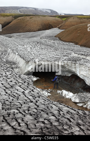 Randonneur regardant dans l'entrée d'une grotte de glace effondrée sur le sentier de randonnée Laugavegur Islande. Banque D'Images