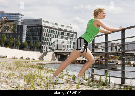 Allemagne, Berlin, young woman stretching on railing, side view Banque D'Images