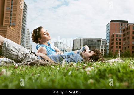 Allemagne, Berlin, Young couple lying in meadow, immeubles de grande hauteur en arrière-plan Banque D'Images