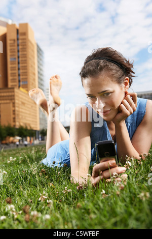 Allemagne, Berlin, young woman lying in meadow using mobile phone, portrait Banque D'Images
