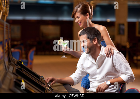 Jeune dame élégante debout, petit ami de jouer slot machine Banque D'Images