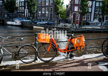 Vélo Orange liés sur Pont sur canal Singel à Amsterdam. Orange est la couleur de la famille royale des Pays-Bas. Banque D'Images