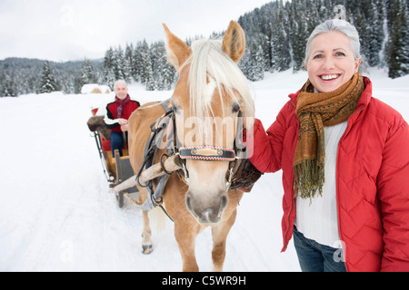 Germany, Berlin, young woman standing by cheval, homme assis en traîneau, smiling, portrait Banque D'Images