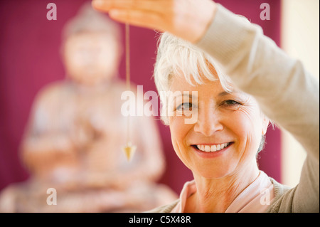 Senior woman holding pendulum, smiling, portrait Banque D'Images