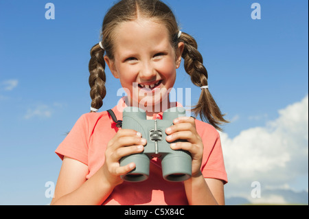 Germany, Girl (6-7) holding binoculars, smiling, portrait, close-up Banque D'Images