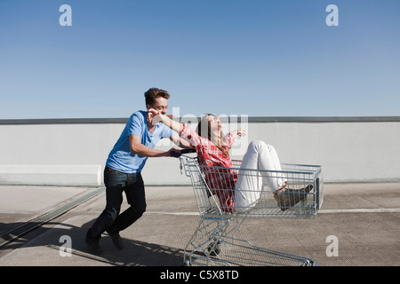 Allemagne, Berlin, Young man pushing woman in shopping cart Banque D'Images