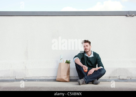 Allemagne, Berlin, jeune homme assis en face de mur, tenant une pomme, portrait Banque D'Images