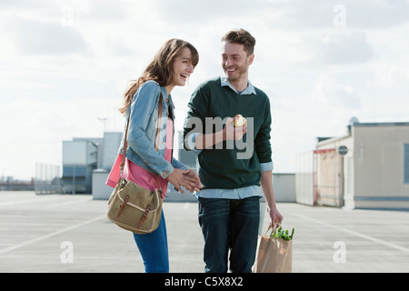 Allemagne, Berlin, young woman standing on niveau parking en riant, l'homme tenant une pomme, portrait Banque D'Images