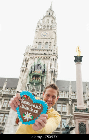 Germany, Bavaria, Munich, Marienplatz, Man holding gingerbread heart, smiling, portrait Banque D'Images