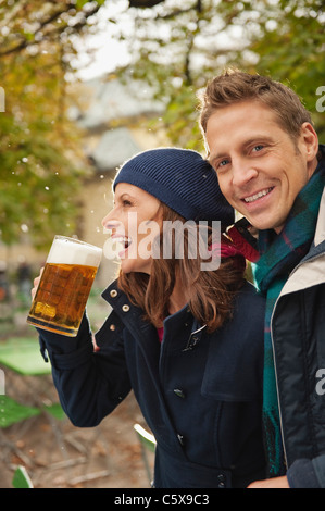 Germany, Bavaria, Munich, en couple dans la région de beer garden, woman holding beer mug, rire, portrait Banque D'Images