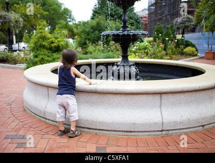 Petit enfant s'appuie sur une fontaine d'eau pour mieux voir Banque D'Images