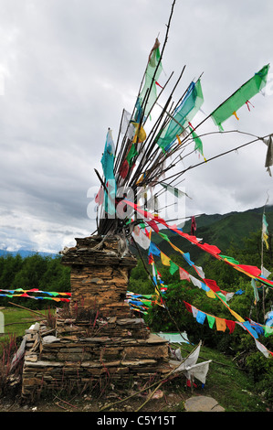 Stupa de pierre et de drapeaux de prière Tibetains. Réserve Naturelle de Siguniang Shan, Sichuan, Chine. Banque D'Images