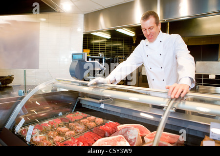 Un boucher à un comptoir de viandes fraîches dans un magasin d'alimentation Banque D'Images