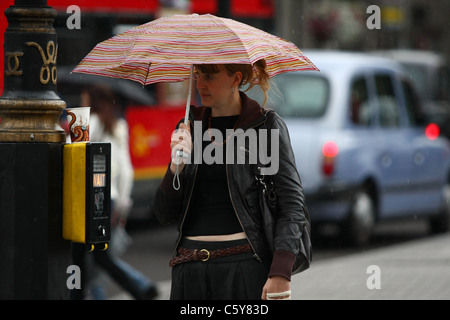 Une dame à l'abri de la pluie sous son parapluie, à Londres, alors qu'elle attend pour traverser une route Banque D'Images